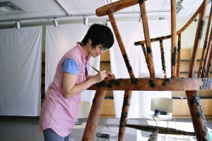 Laura Shintani works on attaching wax fingerprints and initials to one of the seven-foot chairs Oct. 16. (Photo by/ Sean Frame.)